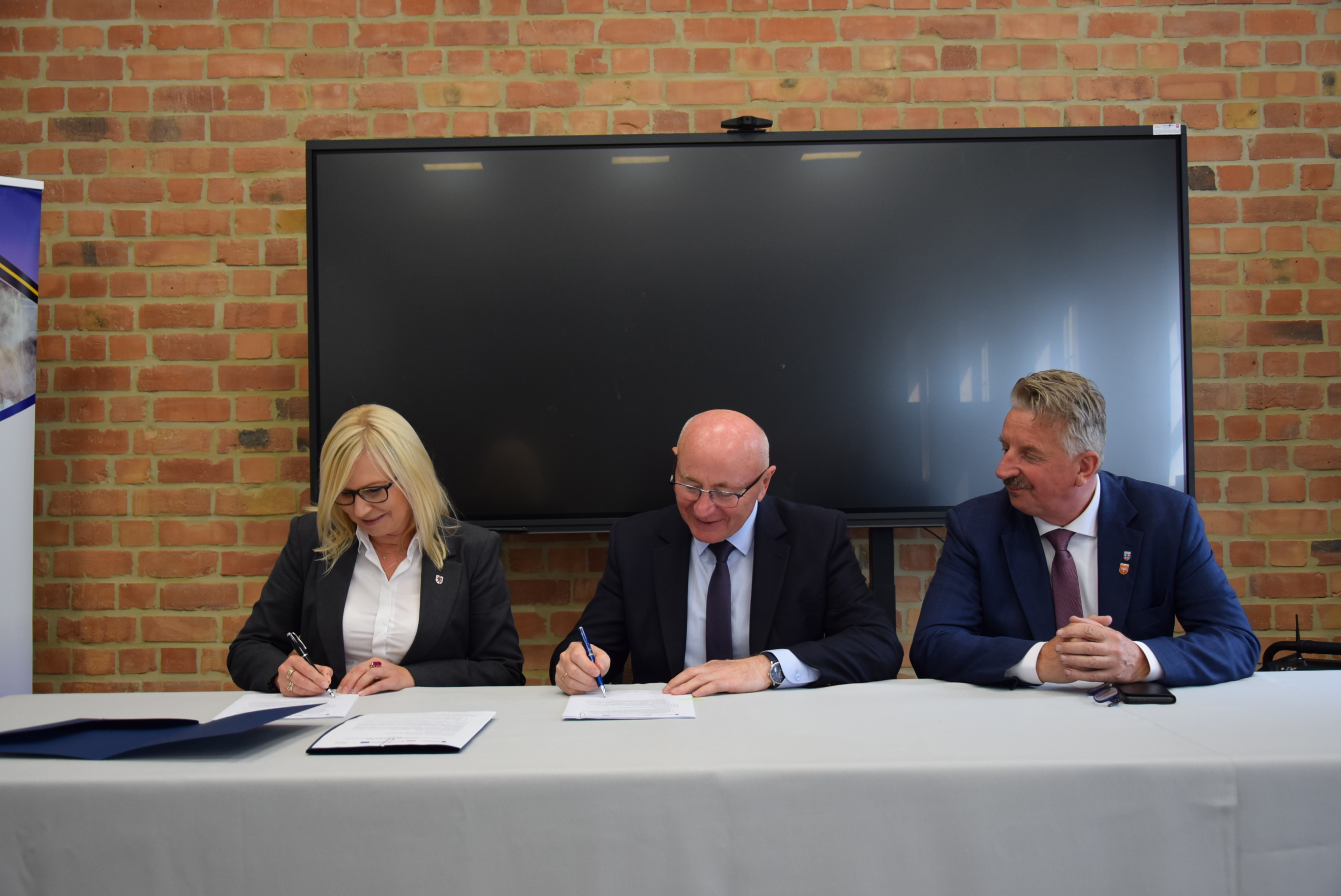 Kolejny zastrzyk funduszy europejskich dla Powiatu Wałeckiego - fot. Starostwo Powiatowe w Wałczu. Strony umowy przy stole prezydialnym podpisują porozumienie - fot. starostwo Powiatowe w Wałczu