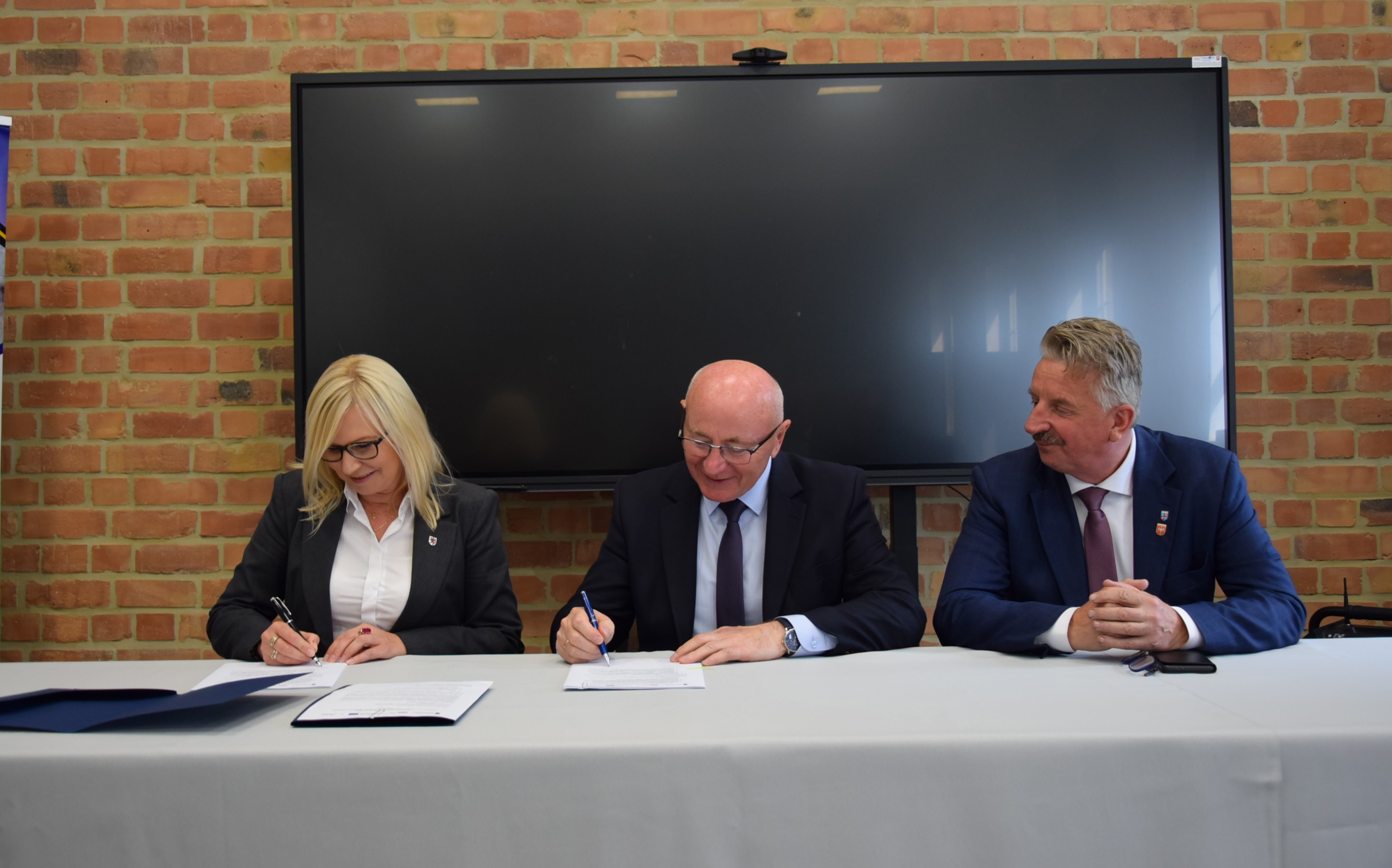 Kolejny zastrzyk funduszy europejskich dla Powiatu Wałeckiego - fot. Starostwo Powiatowe w Wałczu. Strony umowy przy stole prezydialnym podpisują porozumienie - fot. starostwo Powiatowe w Wałczu