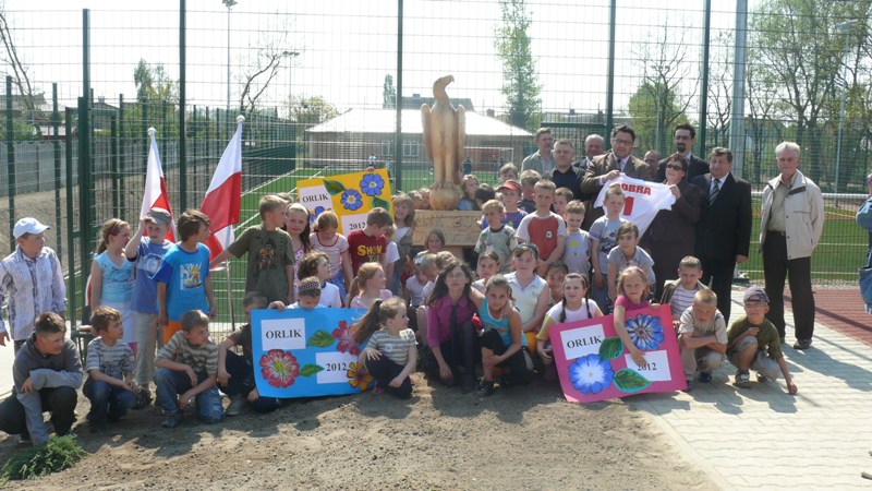 Samorządowcy oraz dzieci przy orle wyrzeźbionym w drewnie