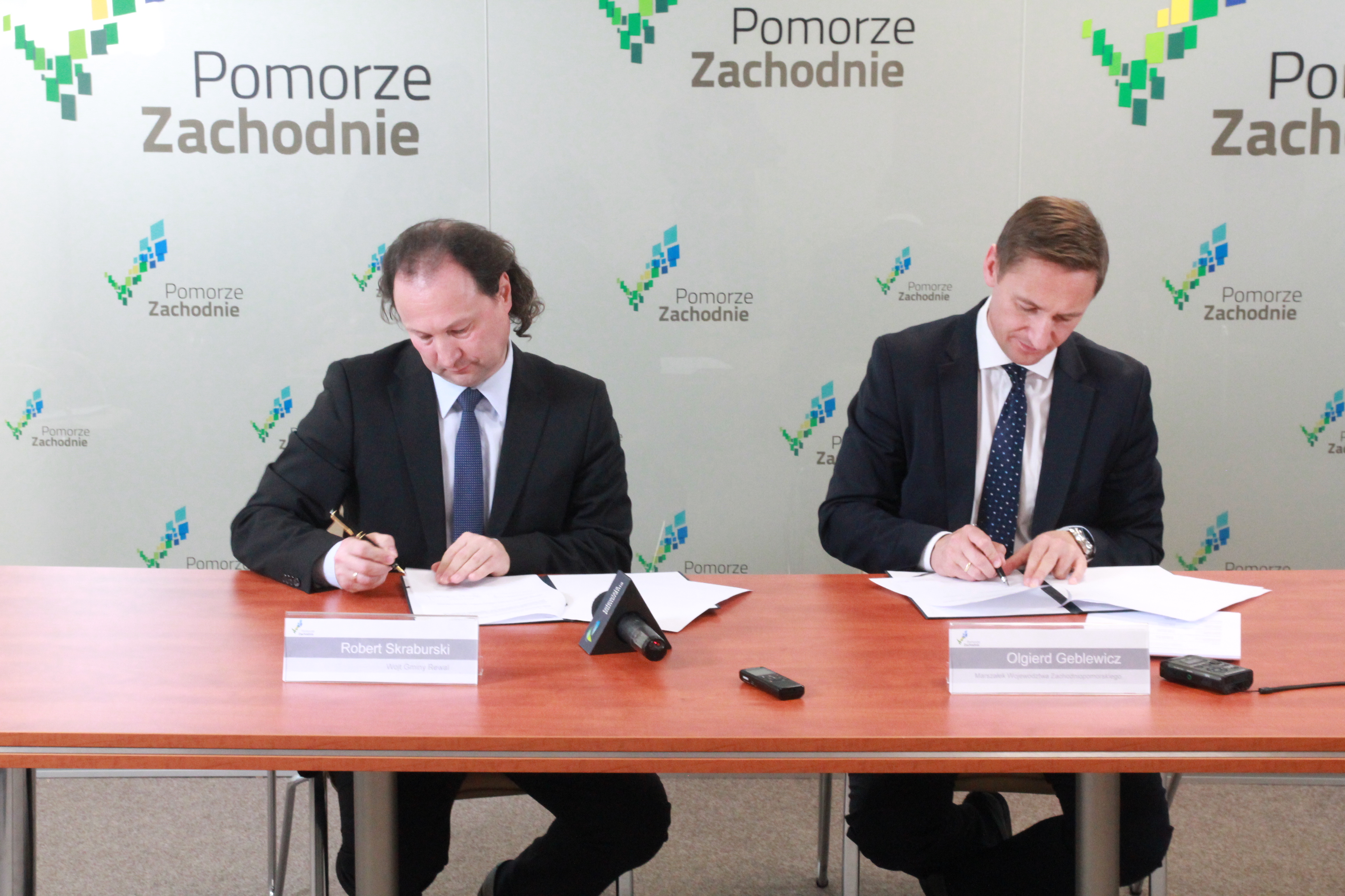 Marszałek Województwa Zachodniopomorskiego Olgierd Geblewicz (z prawej) oraz wójt Rewala podpisują aneks do umowy, na mocy którego zwiększy się dofinansowanie na rewitalizację nadmorskiej kolei wąskotorowej.