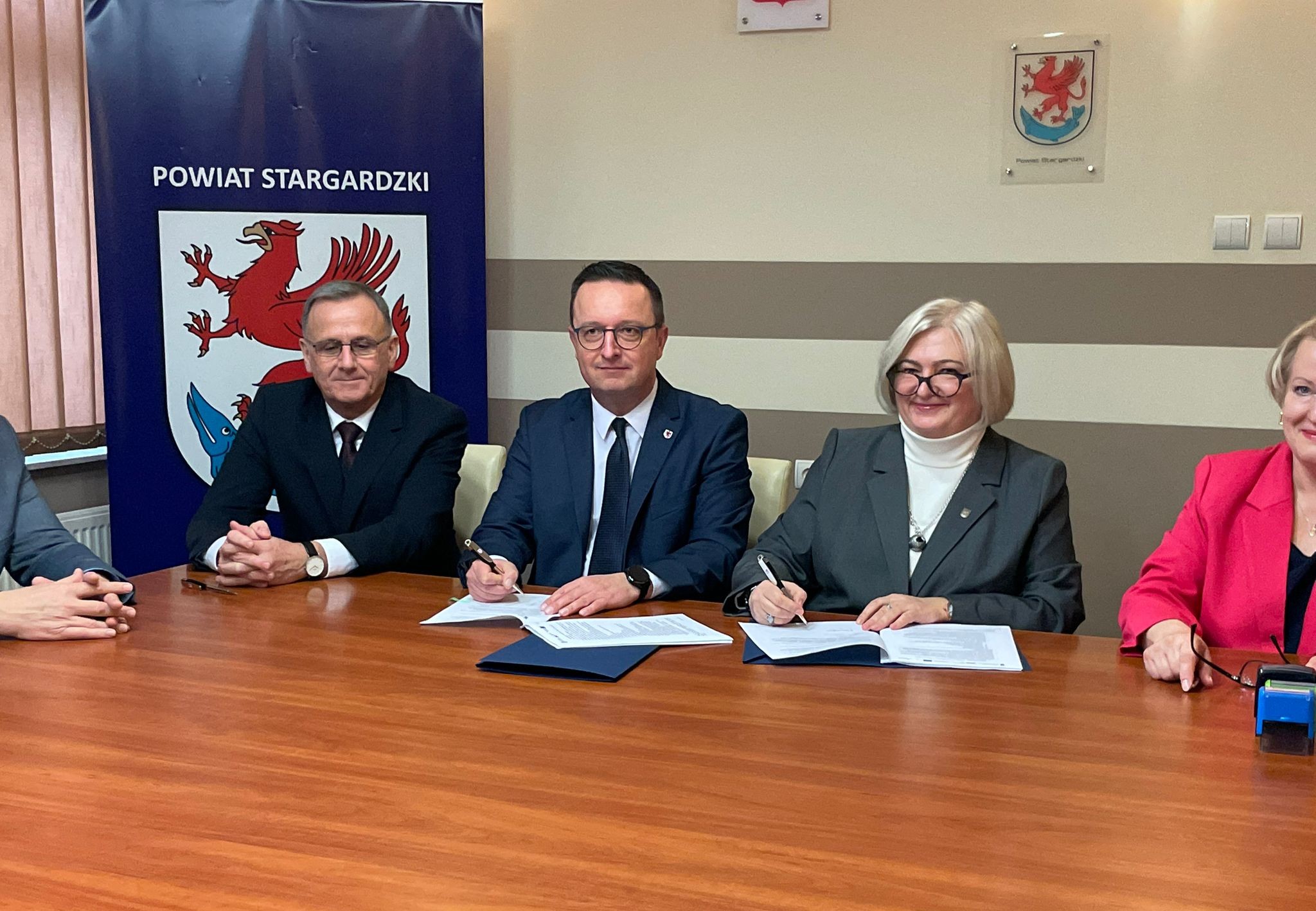 Strony porozumienia podpisują dokument przy stole prezydialnym, obok goście spotkania.