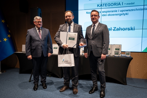 Laureat Rafał Zahorski w towarzystwie organizatirów odbiera nagrodę na scenie. 