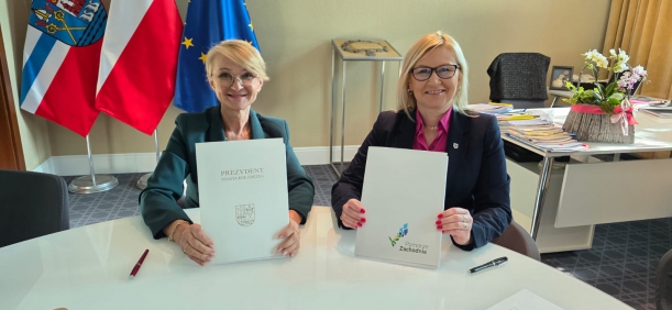 Strony umowy prezentują podpisane porozumienie, stół prezydialny, w tle pomieszczenie biurowe - fot. Urząd Miejski w Kołobrzegu.  