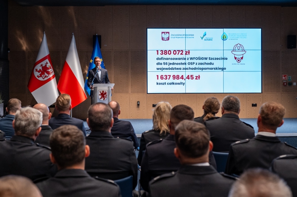 Marszałek Geblewicz przemawia do OSP ze sceny, w tle ekran z informacją o udzielonym wsparciu. 