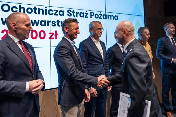 Przedstawiciele OSP odbierają na scenie certyfikaty wsparcia, w tle ekran. 