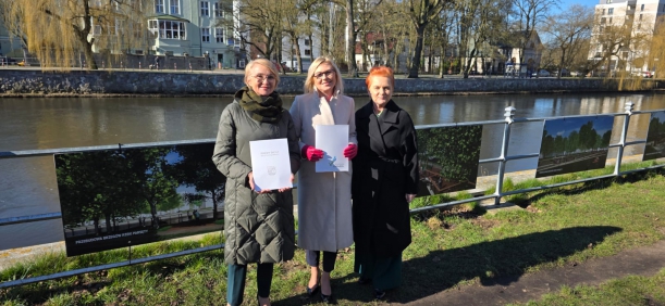 Strony porozumienia prezentują podpisany dokument, w tle brzegi i rzeka Parsęta - fot. Urząd Miejski w Kołobrzegu. 