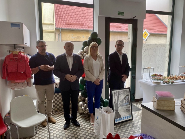 otwarcie sklepu charytatywnego w Wałczu, przy witrynie stoja goście w tym wicemarszałkini i starosta, po prawej stronie widac półki z ubraniami