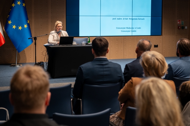 Ważne seminarium dla kadr medycznych. Prof. Małgorzata Serwach siedzi na scenie, w tle telebim z tematyką szkolenia.