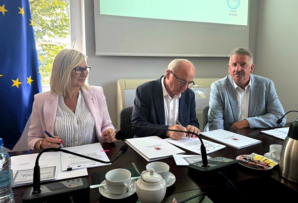 W Mirosławcu powstanie rodzinny dom dziecka. Strony porozumienia podpisują dokument przy stole prezydialnym, w tle okno, flagi i telebim.