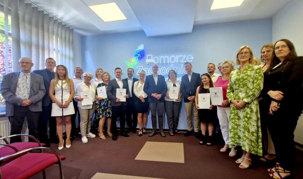 beneficjenci w powiatu koszalińskiego stoją na promocyjnej ściance z marszałekiem i wicemarszałkiem Kowalikiem