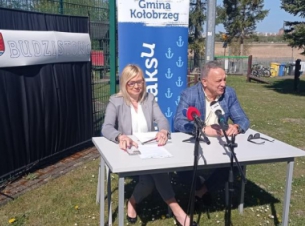 Sygnatariusze umowy podpisują dokument przy stole prezydialnym, w tle obiekt sportowo-rekreacyjny. 