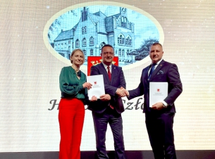 Strony umowy prezentują na scenie podpisane dokumenty, w tle ekran z napisem Człopa.