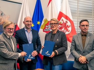 Strony umowy pokazują podpisane porozumienie, w tle flagi, ściana i obraz. 