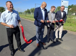 Goście otwarcia wyremontowanej drogi przecinają wstęgę, w tle droga.