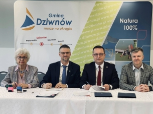 Strony porozumienia składają podpisy na umowie, w tle ścianka promocyjna Gminy Dziwnów. 