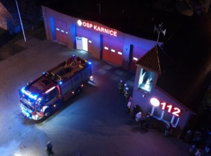 zdjęcie zrionone z drona prezentuje wóz strażacki, pojazd stoi przed remizą, widać napis OSP Karnice oraz numer 112, zdjęcie zrobione w porze nocnej