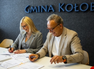 Sygnatariusze umowy podpisują porozumienie przy stole prezydialnym, w tle ściana z napisem Gmina Kołobrzeg. 