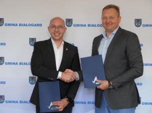 Sygnatariusze umowy prezentują podpisaną umowę, w tle ścianka promocyjna gminy.