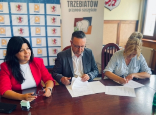 Beneficjenci grantów podpisuja umowy siedząc przy stole prezydialnym. 