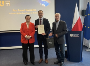 Tomasz Komorowski prezentuje otrzymany dyplom, obok ministra Katarzyna Lubnauer, w tle telebim z nazwą gali.