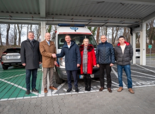 Uczestnicy przekazania ambulansu podczas wspólnego zdjecia stoją przed karetką. 