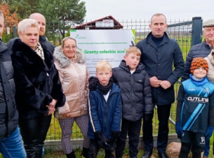 Mieszkańcy Kartlewa i członek Zarządu Województwa Marcin łapeciński stoja przed nowym obiektem sportowo-rekreacyjnym, w tle obiekt. 