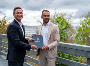 Sygnatariusze umowy prezentuja dokuemnt na kładce, w tle zieleń i Bałtyk. 