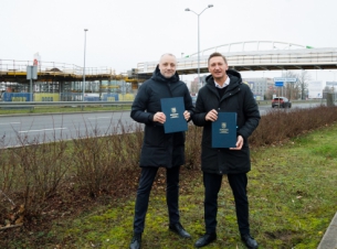 Sygnatariusze umowy prezentują podpisany dokument, w tle budowana kładka nad ul. Struga w Szczecinie. 