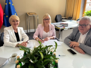 Sygnatariusze umowy podpisują dokument przy stole prezydialnym. 