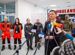 Marszałek Geblewicz przy mikrofinie zabiera głos w sprawie szkoleń dla ratowników medycznych, w tle ambulans szkoleniowy, ratownicy medyczni, grupa interwencyjna Służby Więziennej.
