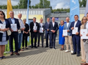 wspólne zdjęcie gości konferencji prasowej przed schroniskiem w Koszalinie, część osób trzyma teczki z umowami 