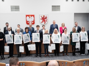 W sali sesyjnej sejmiku województwa marszałek, wyróżnieni i goście pozują do pamiątkowego zdjęcia. 