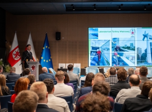 Prof. Jan Drzewieniecki podczas wykładu na scenie, obok ekran ze slajdem z prezentacji. 