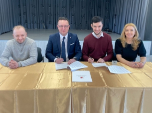 Strony umowy podpisują dokumenty przy stole prezydialnym, w tle scena kinowa.