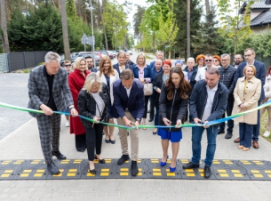 Goście wydarzenia przecinają wstęgę jako symbol zakończenia inwestycji, w tle wyremontowana ulica z poboczami i chodnikami.