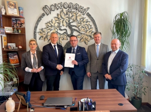 Sygnatariusze umowy prezentują podpisany dokument, w tle sale i herb Nowogard. 