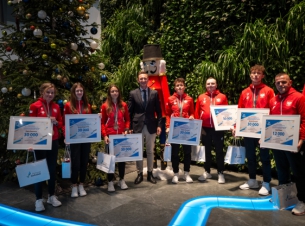 Marszałek Geblewicz i medaliści igrzysk osób niesłyszących pozują z czekami do zdjęcia, w tle choinka i zielona ścinaka. 