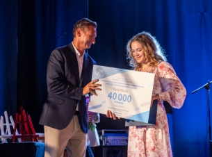 Marszałek Geblewicz wręcza kolarce Darii Pikulik czek z nagrodą finansową, w tle scena i jej aranżacja. 