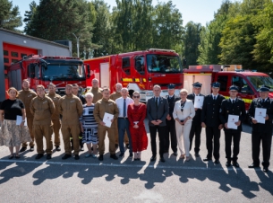Strony umów prezentują na wspólnej fotografii podpisane dokumenty, we tle wozy strażackie.
