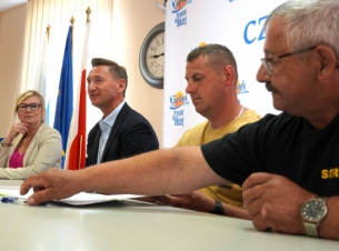 na pierwszym planie strażak sięga po długopis, by podpisać umowę. Obok niego za stołem siedzi drugi strażak oraz marszałek i wicemarszałkini