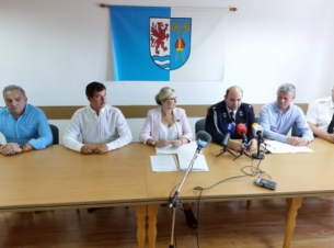 Wicemarszałkini Anna Bańkowska i beneficjenci za stołem prezydialnym podpisują umowy, w tle na ścianie herb powiatu kołobrzeskiego.