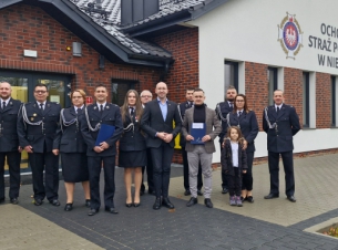 Strażacy i wicemarszałek Jakub Kowalik pozują przed budynkiem OSP w Niedalinie z podpisaną umową. 