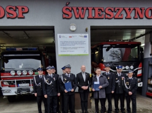 Wicemarszałek Jakub Kowalik i przedstawiciele OSP Świeszyno pozują przed remizą do wspólnego zdjęcia z podpisanymi umowami.