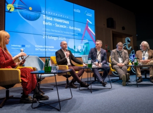 Wicemarszałek Kowalik na siedząco wraz z prowadzącą i partnerami projektu prezentują ze sceny pętlę rowerową Berlin-Szczecin-Kołobrzeg, w tle telebim ze slajdem o pętli. 