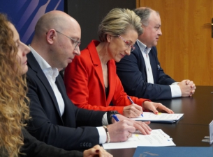 Strony porozumienia podpisują umowę przy stole prezydialnym, w tle ścianka promocyjna uczelni. 