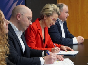 Strony porozumienia podpisują umowę przy stole prezydialnym, w tle ścianka promocyjna uczelni.