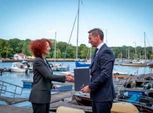 Prezydent Agatowska i marszałek Geblewicz gratulują sobie podpisania umowy, w tle port jachtowy i żaglówki.