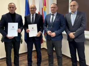 Sygnatariusze umowy prezentują podpisany dokument, w tle flagi i herb Powiatu Łobeskiego.