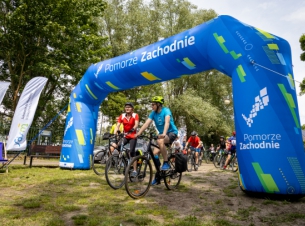 Meta rajdu z uczestnikami, w tle stoiska promocyjne i teren zielony. 