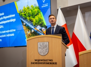 Marszałek Geblewicz przy mównicy mówi o raporcie dotyczącym stanu województwa, w tle ekran ze slajdem. 